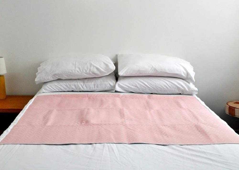 Washable double bed pad protector with tucks on a bed with white pillows and wooden side tables