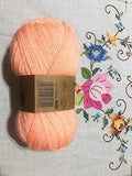 Pale peach double knitting yarn ball made of 100% acrylic placed on floral embroidery fabric