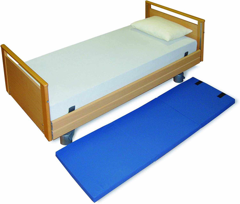 Foldable blue Fall-Out Crash Mat with fastening straps next to a single wooden bed with white mattress and pillow